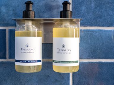 Two bottles of Trevarno natural shampoo and shower gel mounted on a wall with blue tiles at Chi Lowarth in Porthleven