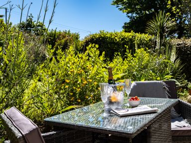 A garden table with a champagne bottle in an ice bucket two glasses a bowl of strawberries and a newspaper at Chi Lowarth in Porthleven