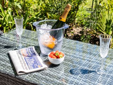 A glass table outdoors with a newspaper bowl of strawberries ice bucket with champagne bottle and two empty champagne flutes at Chi Lowarth in Porthleven
