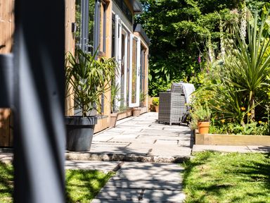 A garden path next to a wooden building with potted plants and outdoor seating at Chi Lowarth in Porthleven