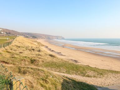A sandy beach with ocean waves and grassy dunes along the coast at Chi Lowarth in Porthleven