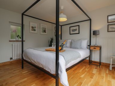 A bedroom with a four-poster bed a bedside table with a lamp and framed pictures on the walls at Chi Lowarth in Porthleven