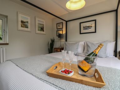 A bedroom with a bed a tray holding a champagne bottle in ice glasses and strawberries at Chi Lowarth in Porthleven