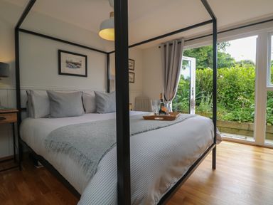 A bedroom with a four-poster bed near a glass door leading to a garden at Chi Lowarth in Porthleven
