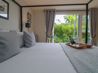 A bedroom with a four-poster bed with grey pillows and sheets and an open door leading to a garden at Chi Lowarth in Porthleven