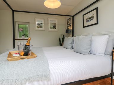 A bedroom with a bed with gray pillows and striped sheets a tray with a bottle in an ice bucket and strawberries on the bed and framed pictures on the walls at Chi Lowarth in Porthleven