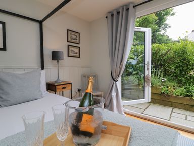 A bedroom with a bed a side table with a lamp a chair and an open door leading to a garden at Chi Lowarth in Porthleven