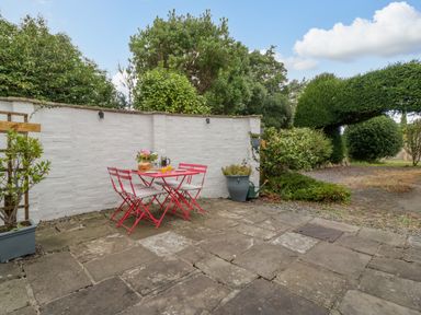 An outdoor patio area with a red table and four chairs a white wall and green plants at Pentre Court Cottage in Abergavenny