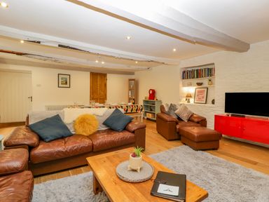 A living room with leather sofas a wooden coffee table a red TV stand and a dining table at Pentre Court Cottage in Abergavenny