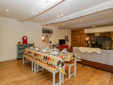 A dining area with a table set with dishes and glasses and benches next to a living room with a sofa and a fireplace at Pentre Court Cottage in Abergavenny