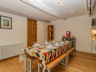 A dining table with a patterned tablecloth set with dishes and glasses in a room with wooden benches and wooden door at Pentre Court Cottage in Abergavenny