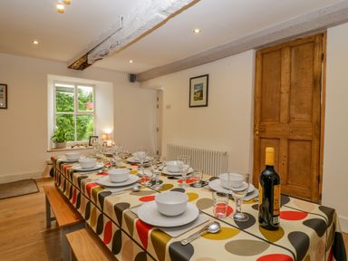 A dining room with a long table set with plates bowls glasses cutlery and a bottle of wine at Pentre Court Cottage in Abergavenny