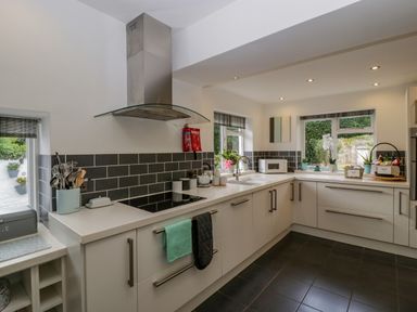 A kitchen with white cabinets black tiled backsplash and various appliances and utensils at Pentre Court Cottage in Abergavenny
