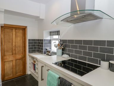 A kitchen corner with wooden door white countertops black tiled backsplash and a stove at Pentre Court Cottage in Abergavenny