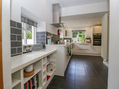 A kitchen with white cabinets grey tiled floor and shelves with books at Pentre Court Cottage in Abergavenny