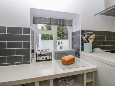 A kitchen counter with a toaster bread box and loaf of bread near a window at Pentre Court Cottage in Abergavenny
