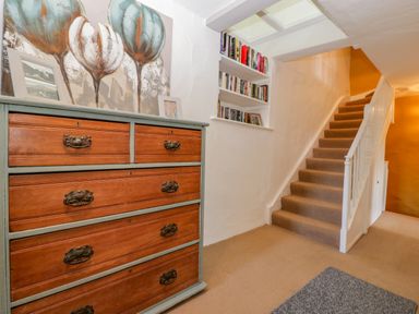 A hallway with a wooden chest of drawers a staircase and shelves with books at Pentre Court Cottage in Abergavenny