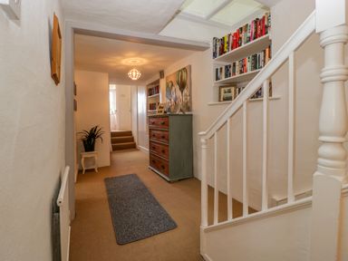 A hallway with stairs a bookshelf a chest of drawers and a small table with a plant at Pentre Court Cottage in Abergavenny