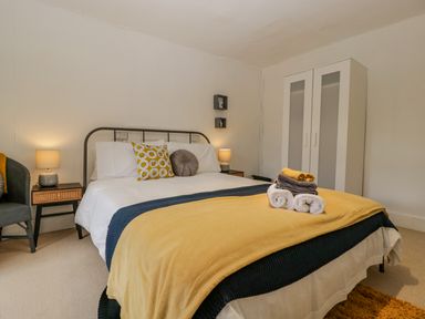A bedroom with a bed that has white linens and yellow and gray pillows with folded towels on top and a wardrobe at Pentre Court Cottage in Abergavenny