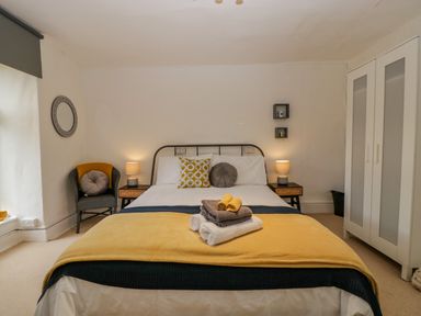 A bedroom with a bed with folded towels and cushions next to bedside tables and a wardrobe at Pentre Court Cottage in Abergavenny