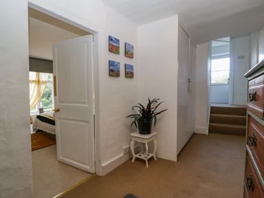 A hallway with a plant on a small table four wall pictures a door to a bedroom and stairs at Pentre Court Cottage in Abergavenny