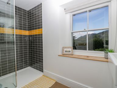 A bathroom with a shower area featuring black tiles with an orange stripe and a window with a wooden ledge holding a small picture frame and a plant at Pentre Court Cottage in Abergavenny