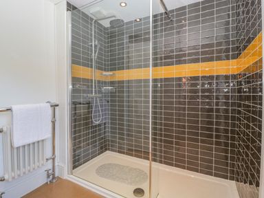 A tiled shower enclosure with a glass door and a towel rail with a white towel at Pentre Court Cottage in Abergavenny
