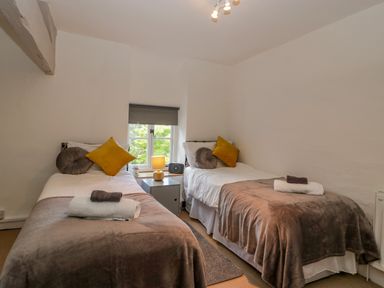 A bedroom with two single beds a window and a bedside table with a lamp and radio at Pentre Court Cottage in Abergavenny