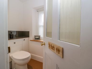 A small bathroom with a toilet a window with a picture frame and a door with a wooden sign at Pentre Court Cottage in Abergavenny