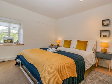 A bedroom with a bed with yellow and blue blankets and two bedside tables with lamps at Pentre Court Cottage in Abergavenny