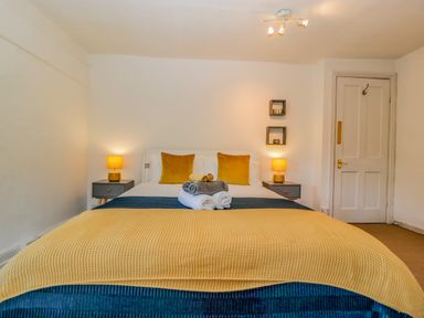 A bedroom with a bed in the center with yellow and blue blankets two bedside tables with lamps and a white door on the right at Pentre Court Cottage in Abergavenny