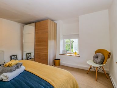 A bedroom with a bed towels on it a wardrobe a chair a window and pictures on the floor at Pentre Court Cottage in Abergavenny