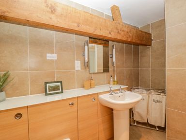 A bathroom with a pedestal sink wooden cabinets a mirror and laundry bags at Pentre Court Cottage in Abergavenny