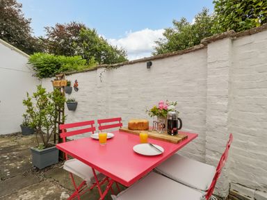 An outdoor patio with a red table and chairs set with orange juice bread and a coffee press at Pentre Court Cottage in Abergavenny