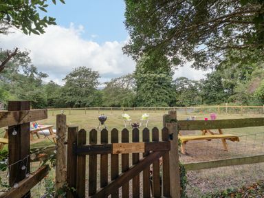 A wooden gate opening to a fenced grassy yard with picnic tables chairs and a barbecue at Pentre Court Cottage in Abergavenny