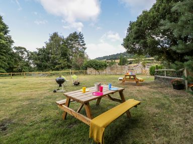 An outdoor garden with picnic tables, a barbecue grill, chairs, and a fenced grassy area at Pentre Court Cottage in Abergavenny