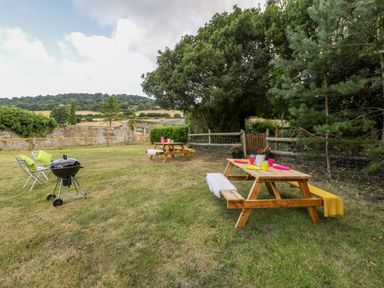 A garden with picnic tables set with plates and cups and a charcoal grill with chairs in a fenced yard at Pentre Court Cottage in Abergavenny