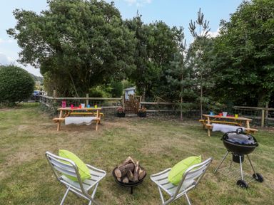 A garden with two metal chairs with green cushions a barbecue and two wooden picnic benches at Pentre Court Cottage in Abergavenny