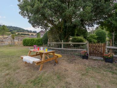 A wooden picnic table with colorful plates and cups in a garden with trees and a wooden gate at Pentre Court Cottage in Abergavenny