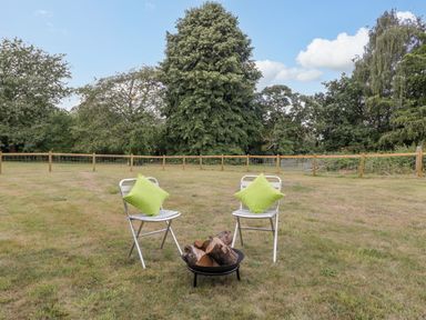 Two chairs with green cushions and a fire pit with logs in a fenced grassy yard at Pentre Court Cottage in Abergavenny