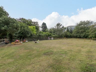 A fenced grassy yard with picnic tables chairs and barbecue surrounded by trees at Pentre Court Cottage in Abergavenny