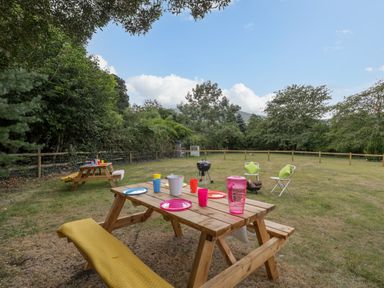 A fenced garden with picnic tables and chairs around a barbecue grill at Pentre Court Cottage in Abergavenny