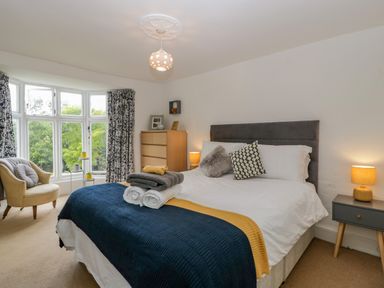 A bedroom with a double bed a chest of drawers an armchair and a bay window at Pentre Court Cottage in Abergavenny