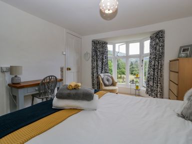 A bedroom with a bed chair desk and chest of drawers next to a window at Pentre Court Cottage in Abergavenny