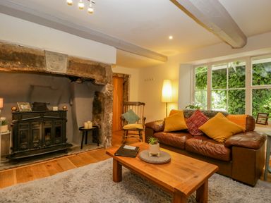 A living room with a leather sofa cushions a wooden coffee table and a fireplace at Pentre Court Cottage in Abergavenny