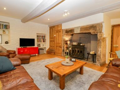 A sitting room with leather sofas a wooden coffee table a tv on a red cabinet and a fireplace at Pentre Court Cottage in Abergavenny