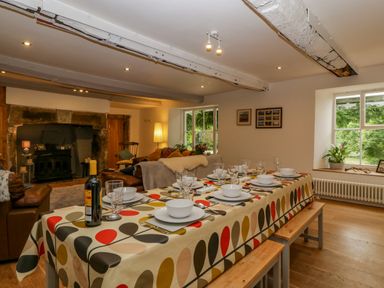 A dining table with tableware and a bottle of wine next to a living area with sofas and a fireplace at Pentre Court Cottage in Abergavenny