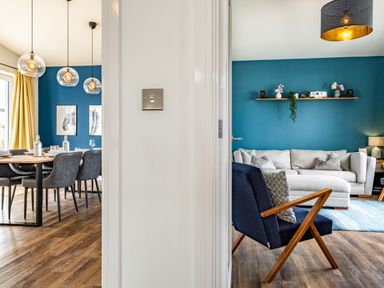 A dining area with a wooden table and chairs next to a living room with a sofa and armchair at Beach Haven in Perranporth