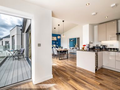 An open plan kitchen and dining area with wooden flooring and a small balcony with a table and two chairs at Beach Haven in Perranporth