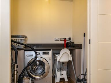 A laundry room with a washing machine a vacuum cleaner a laundry basket a high chair and cleaning tools at Beach Haven in Perranporth